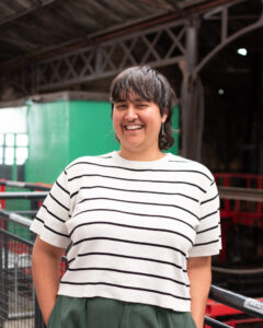 An adult with a medium skin tone, dark-brown shoulder length hair, and a white t-shirt with black horizontal stripes.