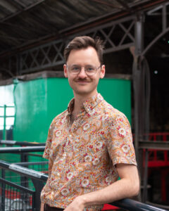 An adult with light skin, short brown hair, glasses, and a patterned yellow shirt.