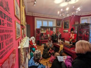 A room full of children and adults are gathered around a person dressed as Santa Claus.