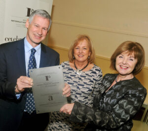 Three adults smiling and holding a plaque.