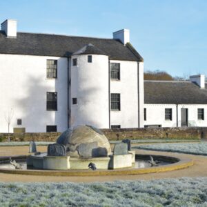 A large three-storey building with white walls and a ark grey slate roof. Frost covers a fountain and lawn in front of the building.